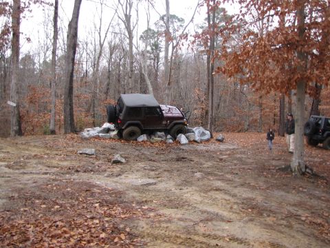 1979 Ford Bronco - A dark red Jeep Wrangler is positioned on a pile of rocks in a wooded area, with another Jeep visible in the background.