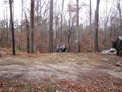 1979 Ford Bronco - Two Jeeps are seen in a wooded area with one driving up a dirt incline.