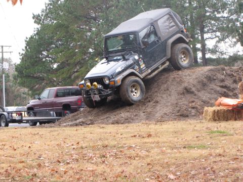 1979 Ford Bronco - A black Jeep Wrangler navigates an off-road obstacle, while a red pickup truck and trailer wait nearby.
