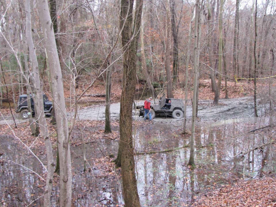 Two Jeeps navigating a muddy forest trail with standing water