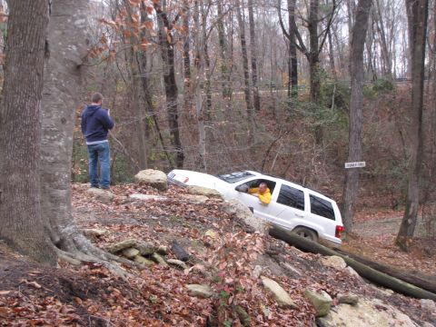 1979 Ford Bronco - A white SUV navigates a challenging off-road trail in a wooded area.