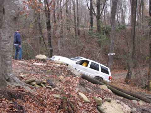 1979 Ford Bronco - A white SUV navigates a challenging off-road course in a wooded area.