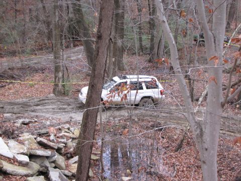 1979 Ford Bronco - A white SUV is seen driving through a muddy, wooded area on an off-road trail.