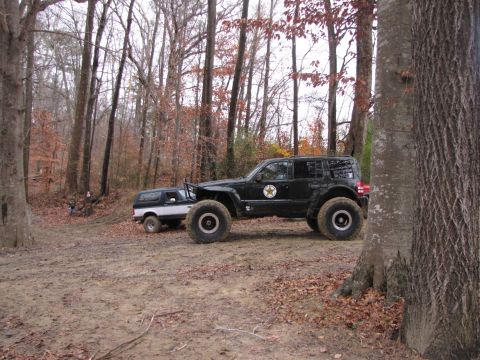 1979 Ford Bronco - Two modified SUVs are parked in a wooded area during the fall season.