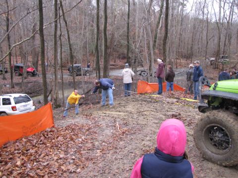 1979 Ford Bronco - Several off-road vehicles are present in a muddy, wooded area with people attempting to assist them.