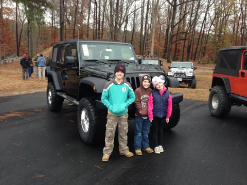 1979 Ford Bronco - Three children pose in front of a black Jeep Wrangler, with other Jeeps in the background.