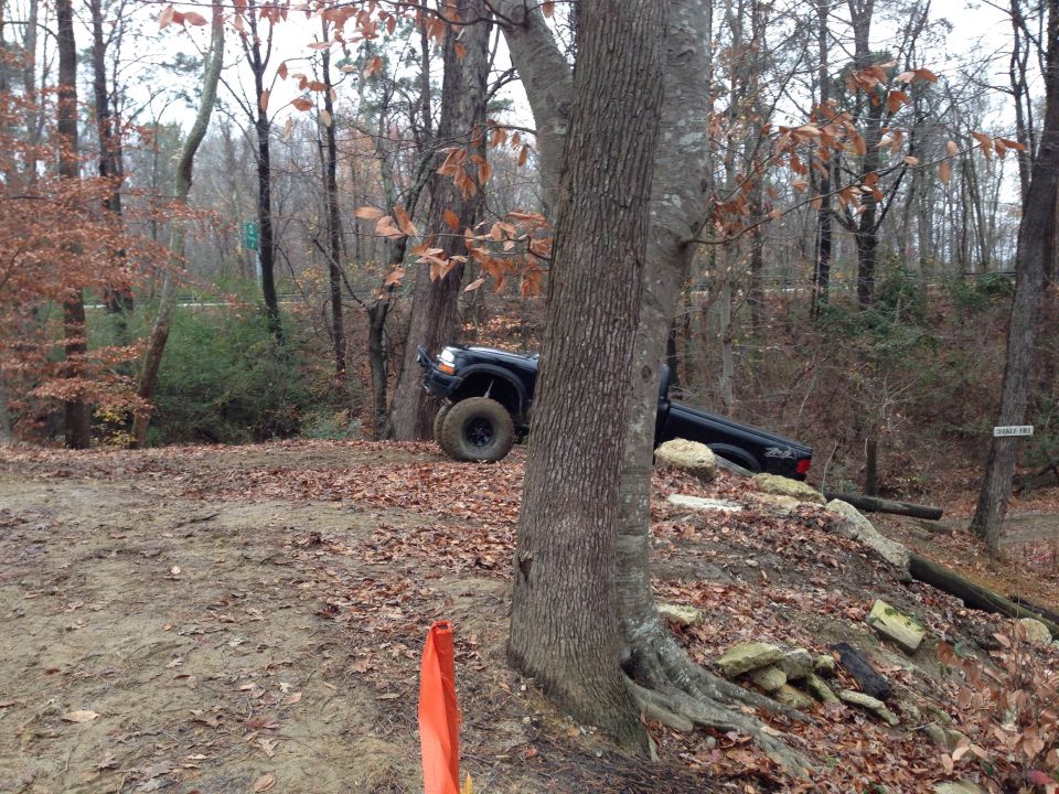 Black pickup truck tilted on a wooded trail, front wheel turned