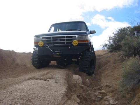 1994 Ford Bronco - A modified Ford Bronco navigates a steep, rocky off-road path under a cloudy sky.