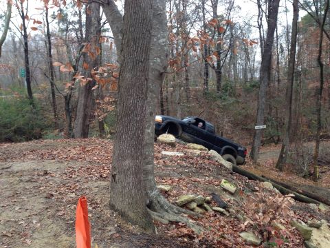 1979 Ford Bronco - A black pickup truck is shown driving off-road on a challenging terrain with trees and rocks surrounding it.
