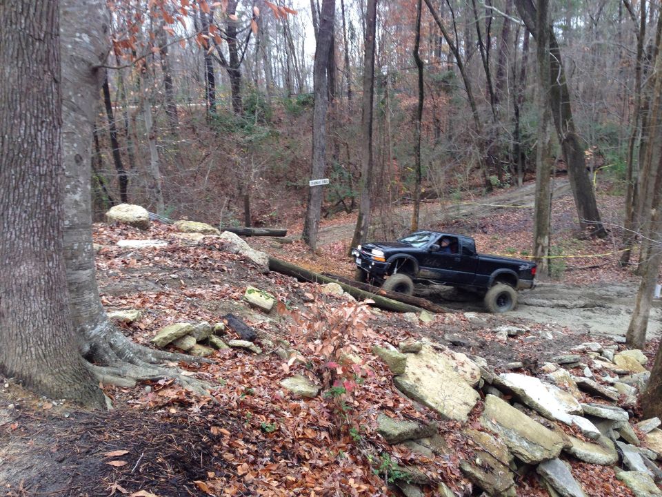 Black pickup truck with large tires navigating a wooded off-road course