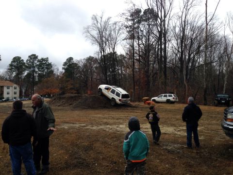 1979 Ford Bronco - A white SUV is positioned on a dirt mound while onlookers observe the scene.