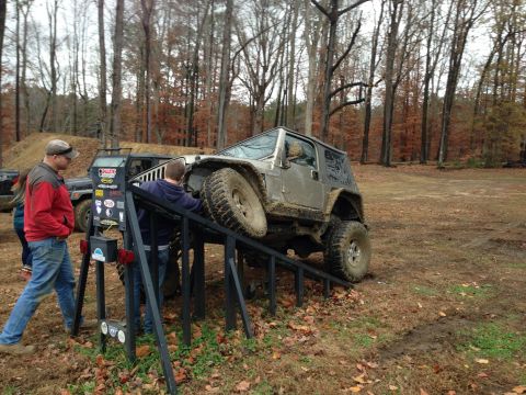 1979 Ford Bronco - A silver Jeep Wrangler navigates an off-road obstacle course with assistance from onlookers.