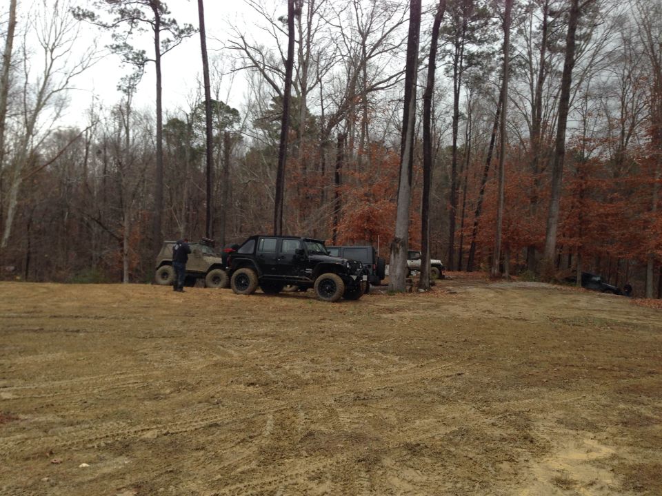 Several off-road vehicles parked in a muddy clearing surrounded by trees