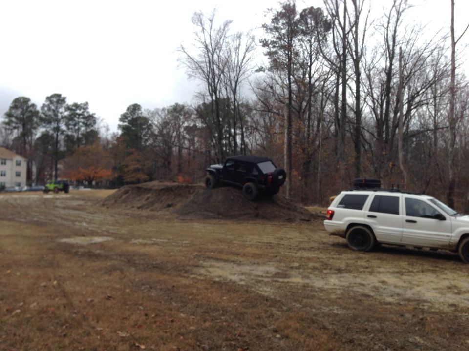 black SUV climbing dirt mound, white SUV parked nearby, green Jeep in background