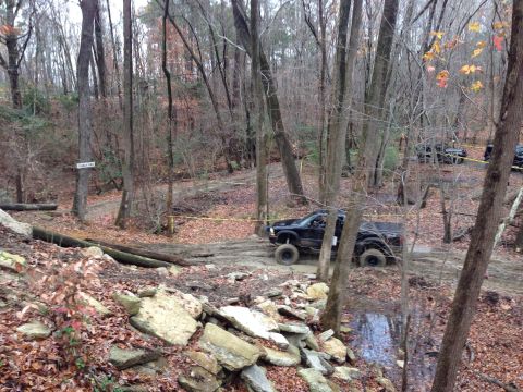 1979 Ford Bronco - A black pickup truck is seen traversing a challenging off-road course through a dense forest.