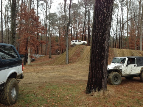 1979 Ford Bronco - Several off-road vehicles are gathered in a wooded area with dirt mounds for off-roading.