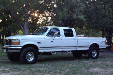 1997 Ford F-350 - A white crew cab pickup truck is parked on a grassy area with trees behind it.