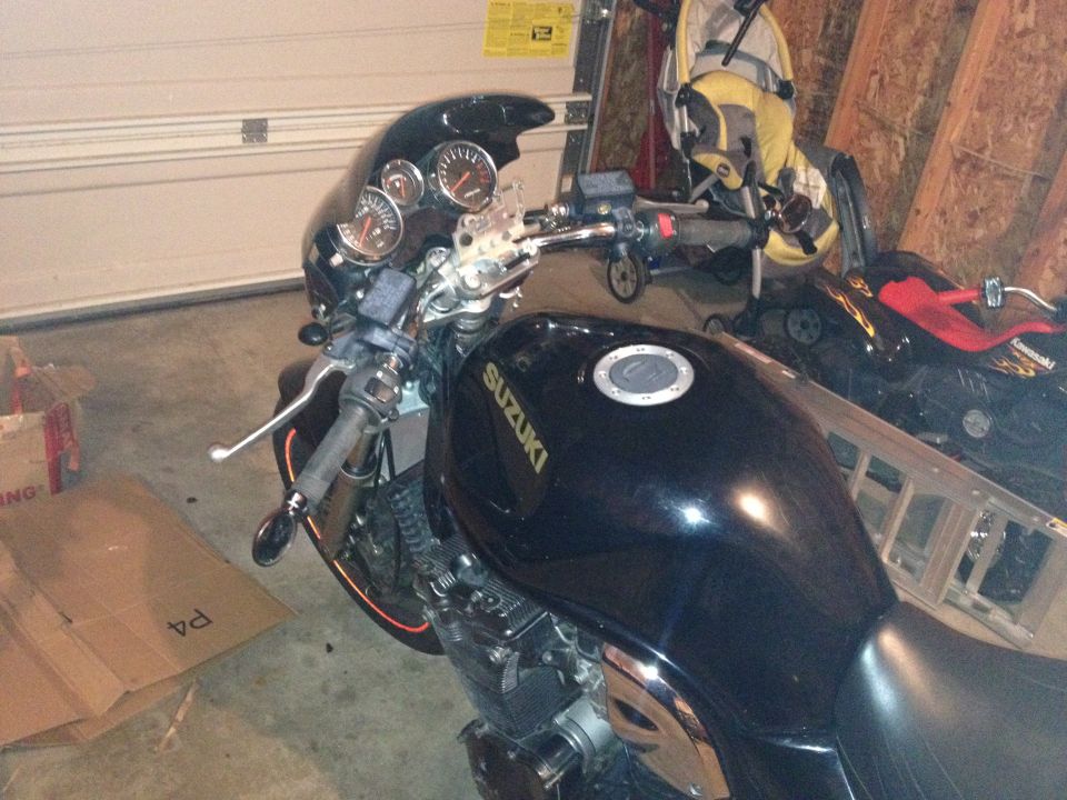 Black Suzuki motorcycle in garage with gauges and handlebars visible