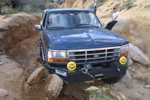 1994 Ford Bronco - A blue Ford Bronco is shown navigating a challenging off-road trail with rocky terrain.