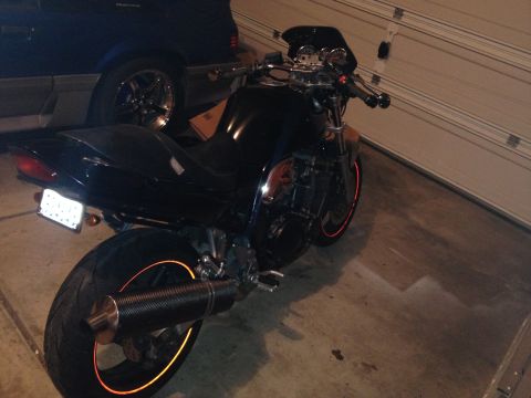 1998 Suzuki Bandit - A black motorcycle with orange rim accents is parked in a garage next to a car.