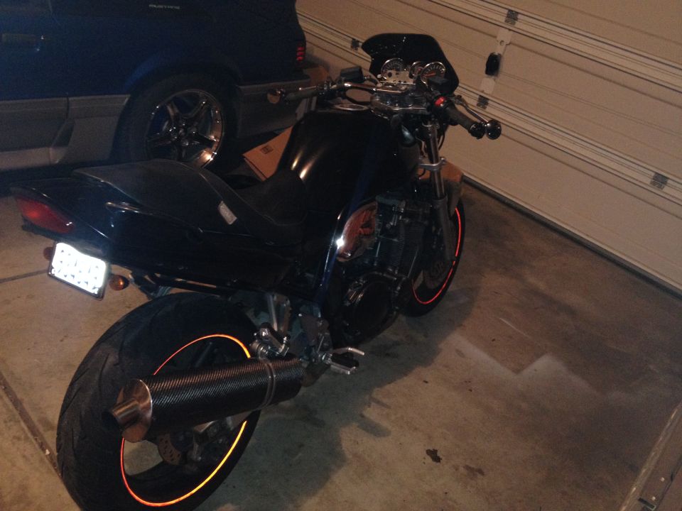 Black motorcycle with orange rim accents parked next to a dark blue car in a garage