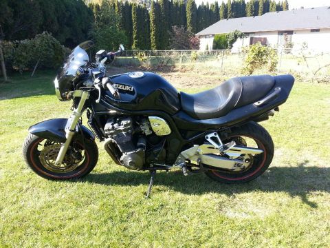 1998 Suzuki Bandit - A black Suzuki motorcycle is parked on a grassy lawn with a house and trees in the background.