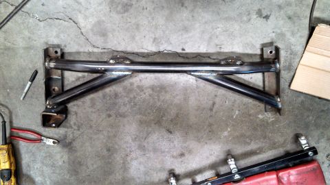 1967 Ford F-250 - A custom-fabricated metal crossmember is shown on a workshop floor, surrounded by tools and materials.