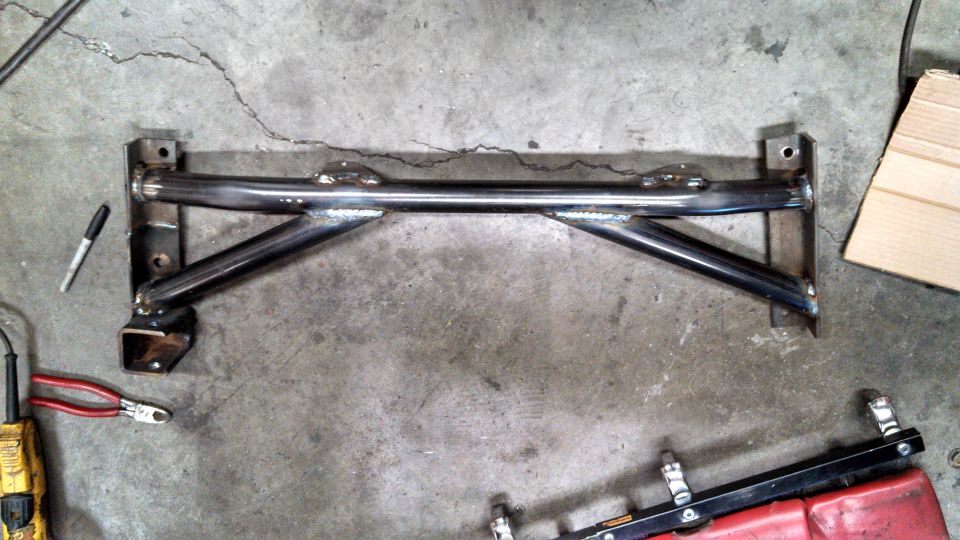 Custom metal crossmember with welded joints, lying on a concrete floor next to tools