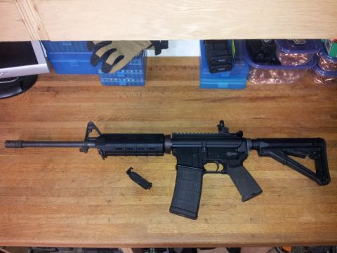 1996 Ford Bronco - AR-15 style rifle with accessories on a wooden table, next to storage containers.