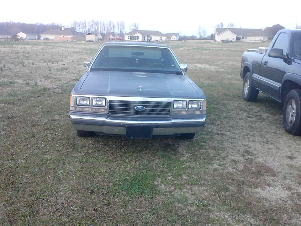 1980s Ford sedan parked on grass next to a pickup truck