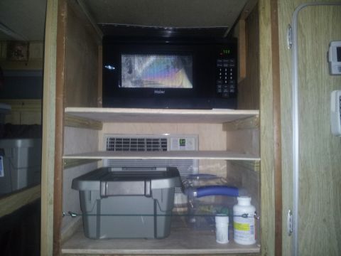 1986 Ford Bronco - Shelving unit inside a vehicle holds a microwave, storage containers, and various bottles.