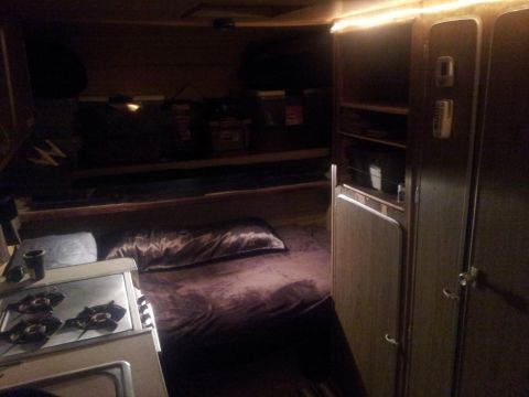 1986 Ford Bronco - Camper van interior features a bed, a two-burner stove, and storage cabinets.