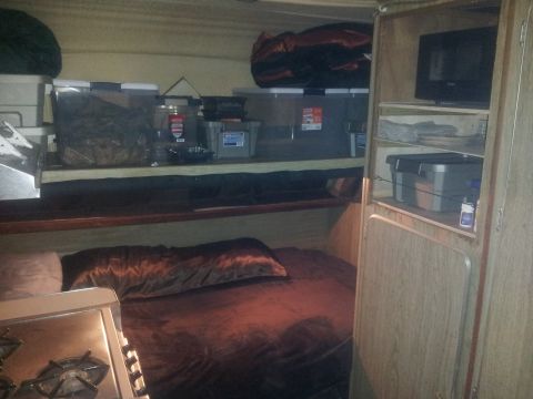 1986 Ford Bronco - The interior of a recreational vehicle shows a made bed, storage solutions, and a small television mounted on a shelf.