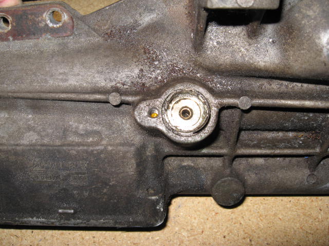 Close-up of a cast metal automotive part with a threaded fitting and a small yellow plug