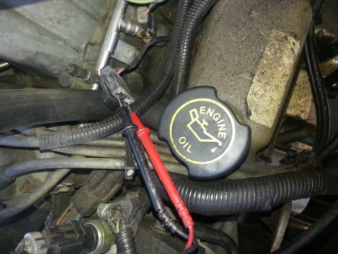 1994 Ford Bronco - Multimeter probes are connected to an engine sensor, with an oil cap nearby.