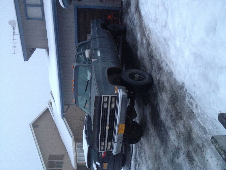 Dark-colored pickup truck with a dually rear axle, parked in snow. Visible front grille and headlights