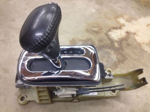 1998 Ford Crown Victoria - Side view of an automatic shifter assembly showing the leather knob, chrome PRND bezel and plastic base on concrete.