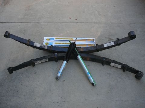 1988 Ford Bronco - Leaf springs and shock absorbers are displayed on a concrete surface, with product boxes in the background.