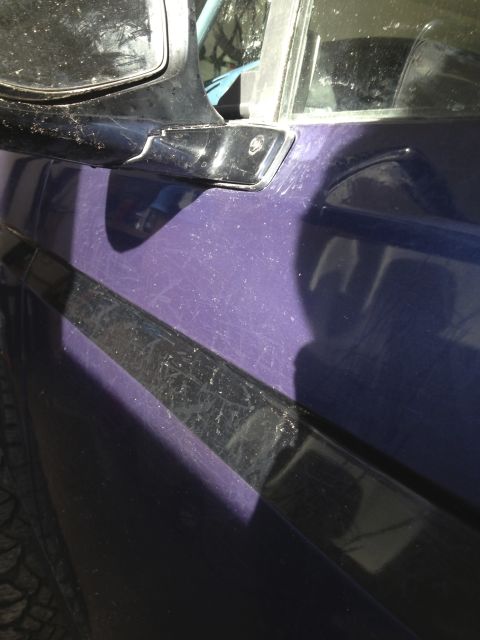 1996 Ford Bronco - Side view of a purple vehicle black trim and a chrome accent near the side mirror.