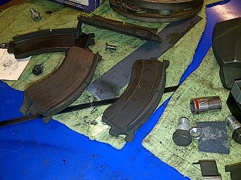 1995 Ford Probe - Two used brake pads are laid out on a light green shop towel next to various bolts, a nut, and a socket. The brake pads show significant we…