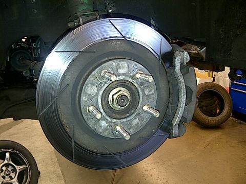 1995 Ford Probe - A close-up view of a car's front brake rotor and caliper assembly, showing slotted rotor design and a tire in the background.