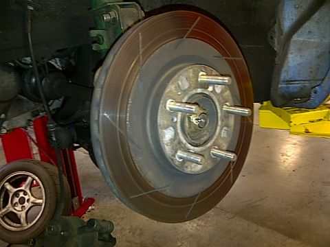 1995 Ford Probe - A close-up view of a car's brake rotor and hub assembly, with a red jack stand visible underneath the suspension components. A spare tire i…