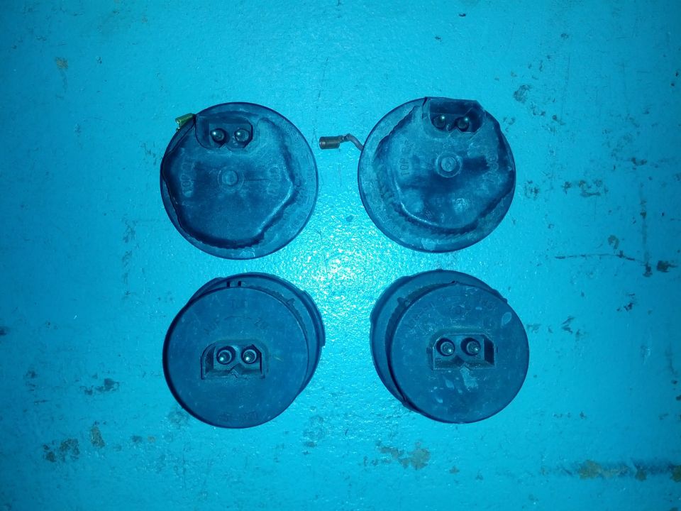Four black circular automotive horns on a blue surface