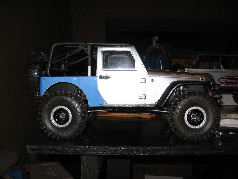 RC Jeep Wrangler with silver body, blue rear accents, black roll cage, and off-road tires.