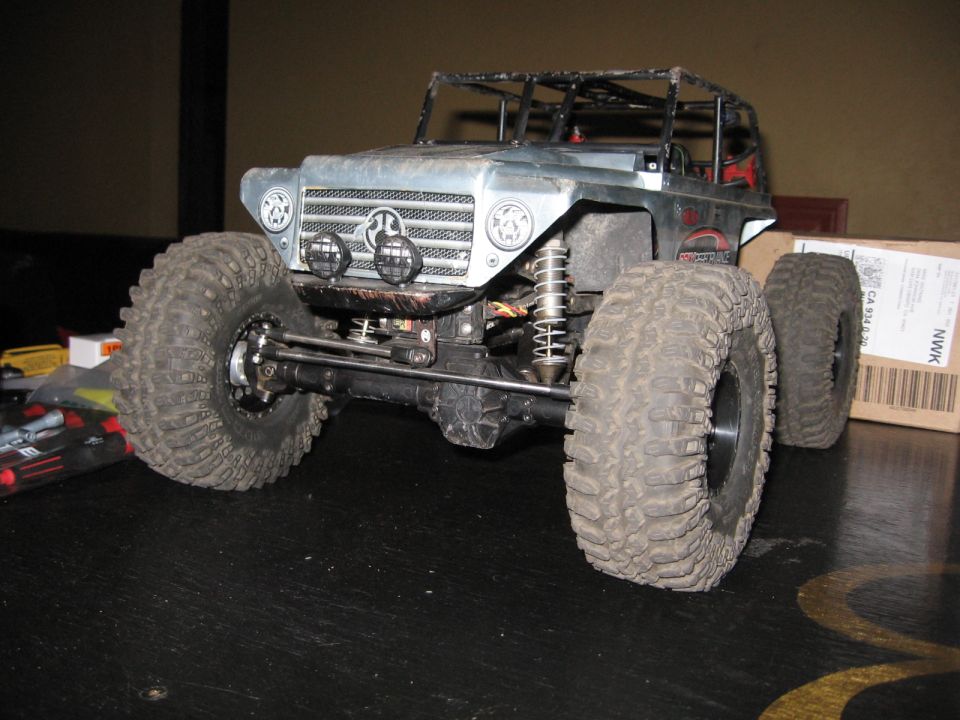 Silver RC rock crawler with large tires and roll cage, front 3/4 view.