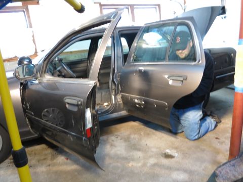 1991 Ford LTD Crown Victoria - Photograph of a person performing repair work on a gray sedan, not a document.