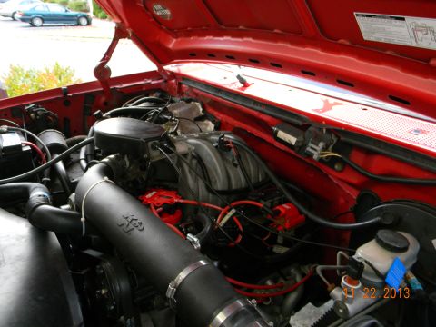 1995 Ford Bronco - The hood of a red Ford Bronco is open, revealing the engine bay. A K&N air intake system is visible, along with various engine components a…