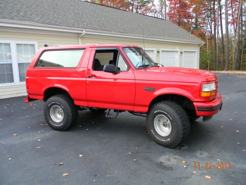 1995 Ford Bronco - A bright red 1995 Ford Bronco is parked on a paved driveway in front of a house with a garage. The vehicle is shown from the side with larg…