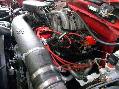 1995 Ford Bronco - Close-up view of the engine bay of a red Ford Bronco, showcasing a K&N air intake system, red spark plug wires, and a red distributor cap.…