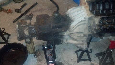 1988 Ford Bronco - An engine and transmission assembly is supported by jack stands and a hydraulic jack on a concrete floor. A drain pan is positioned nearby.